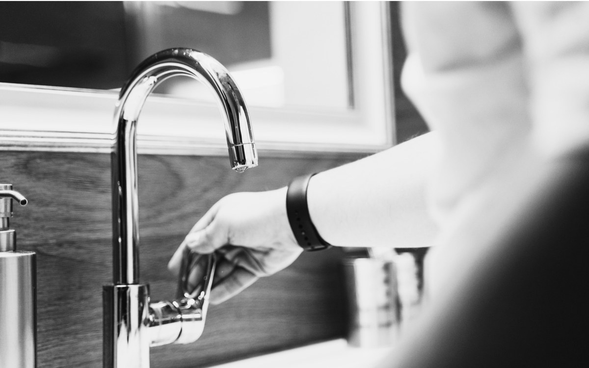 A hand turning on a chrome tap